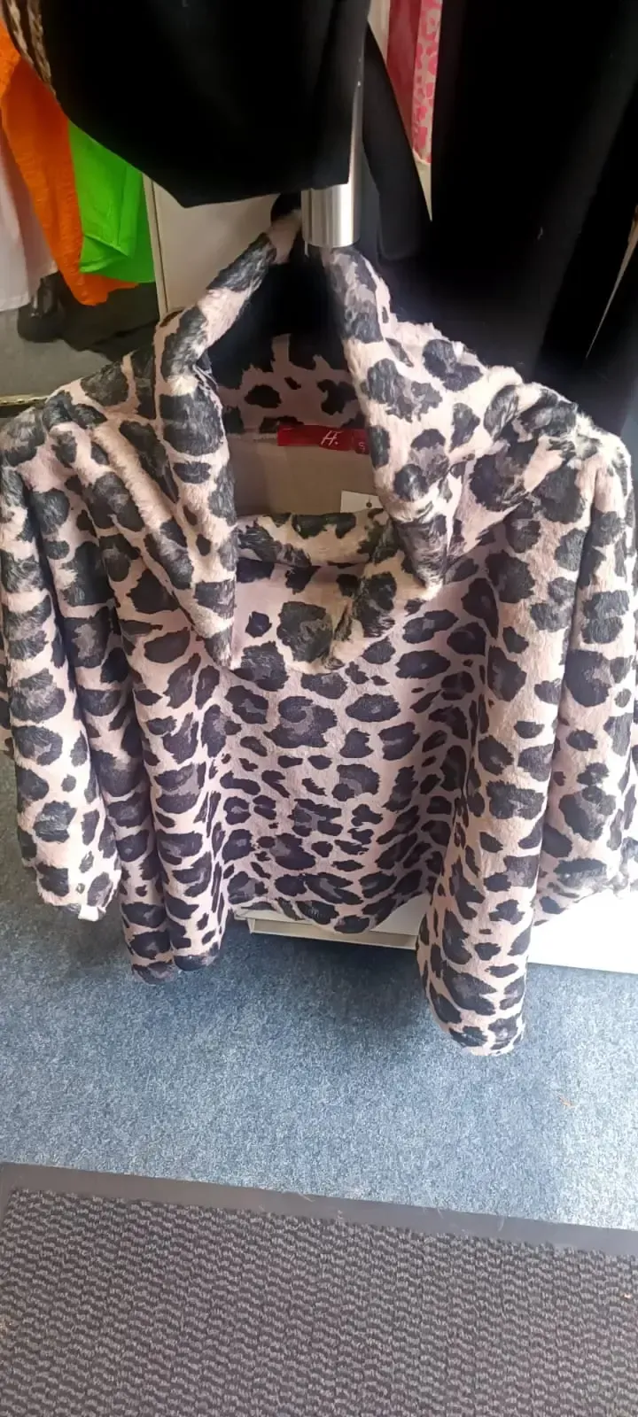 Ein Hoodie mit Leopardenmuster hängt an einem Kleiderständer in einem Geschäft.