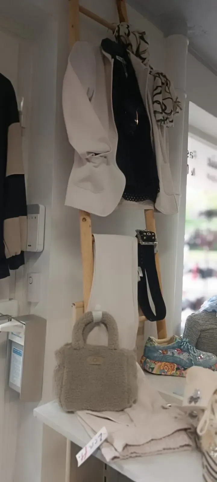 Kleiderständer mit weißen und schwarzen Jacken, hängenden Accessoires und einer grauen Handtasche in einer Boutique.