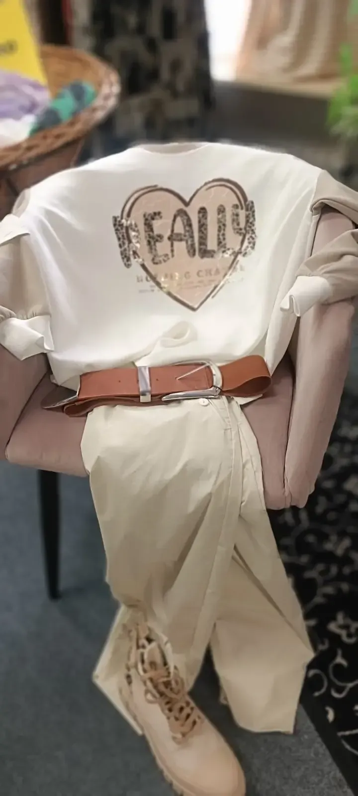 Weißes T-Shirt mit „FALO“-Herzmotiv, hellbraune Hose und brauner Gürtel auf einer Schaufensterpuppe.