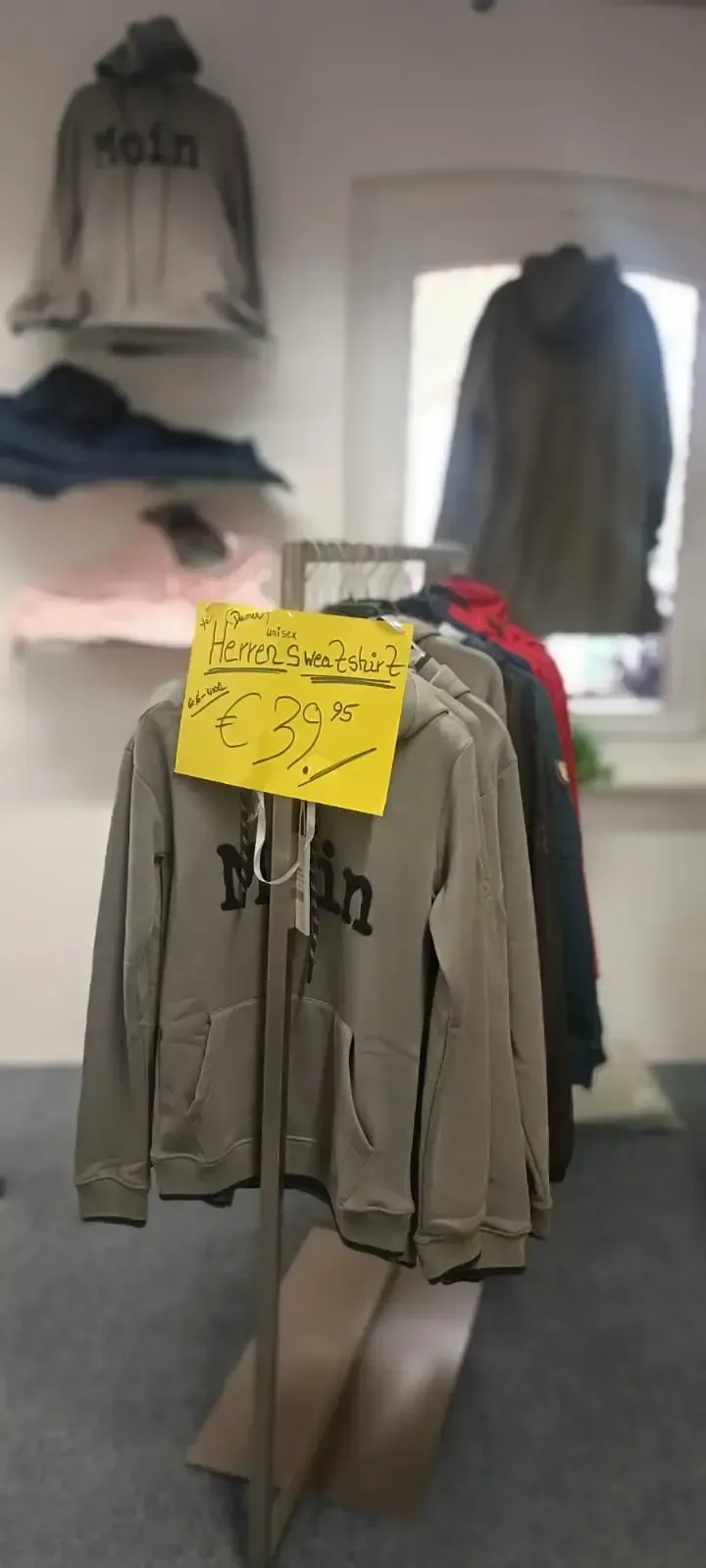 Kleiderständer mit einer hellbraunen Jacke auf einem Kleiderbügel und anderen Kleidungsstücken auf Wandregalen in einem Zimmer