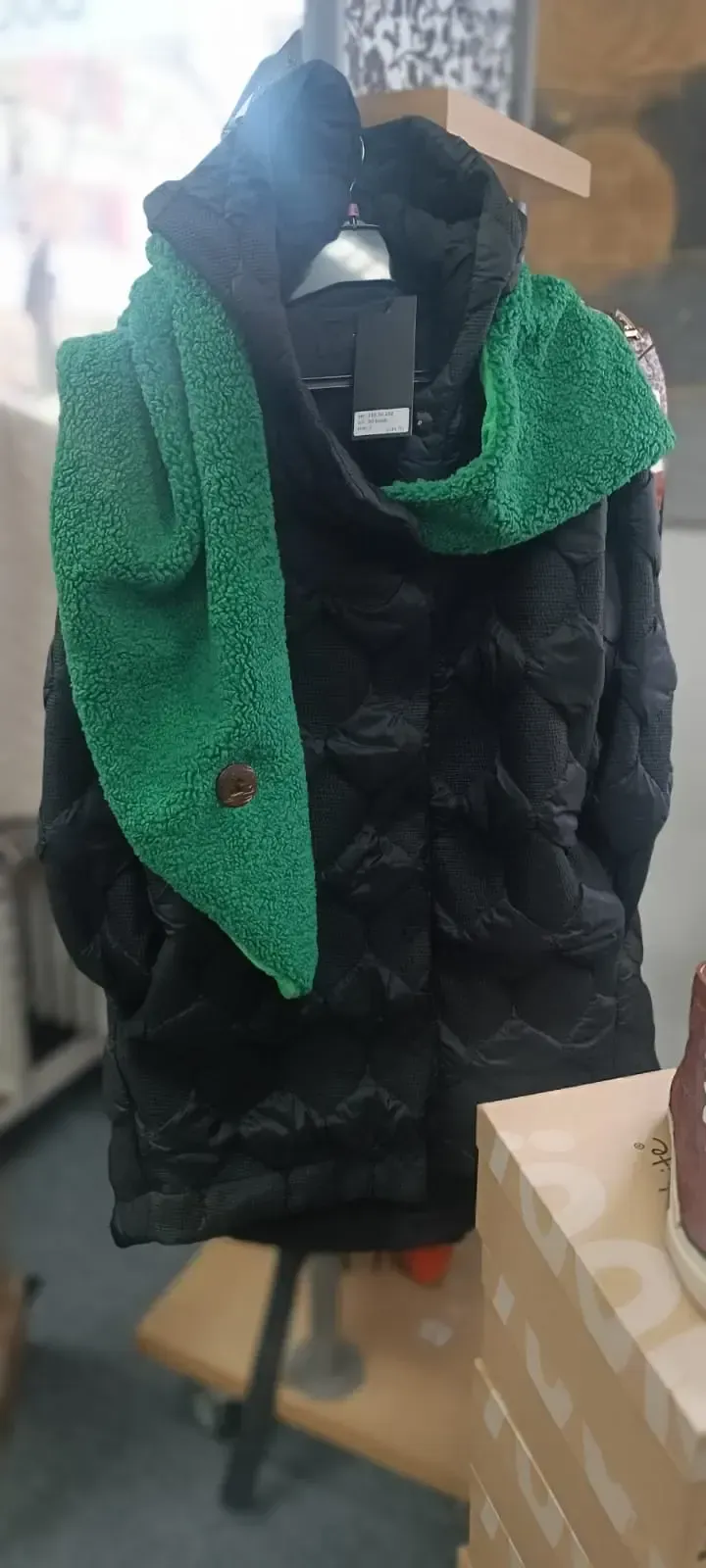 Schwarze Steppjacke an einer Schaufensterpuppe, über deren Schultern ein grüner, strukturierter Schal drapiert ist.
