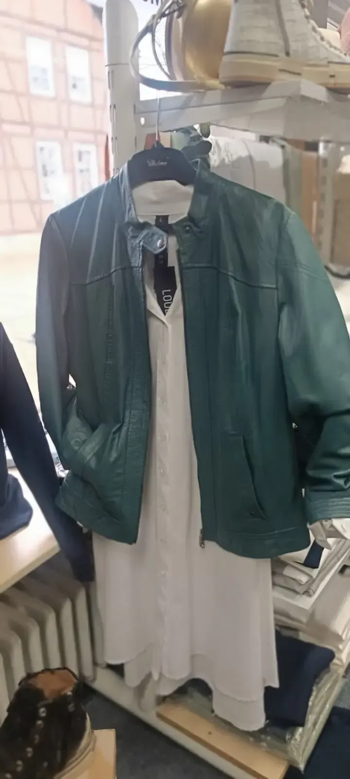 Grüne Jacke über weißem Kleid auf einem Kleiderständer im Schaufenster
