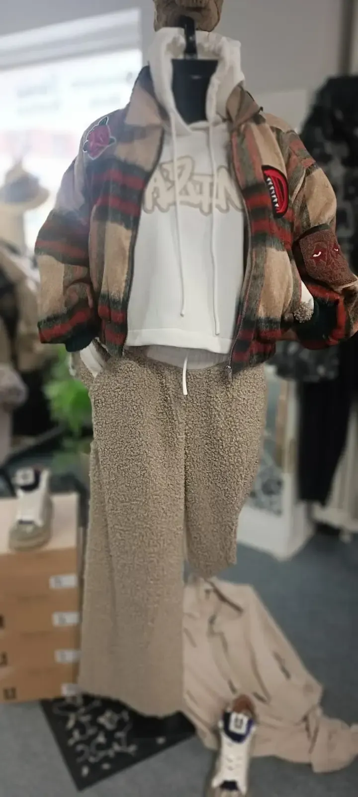 Schaufensterpuppe in einem Bekleidungsgeschäft, die eine karierte Jacke, einen weißen Kapuzenpullover, eine gemusterte Hose und Turnschuhe trägt.