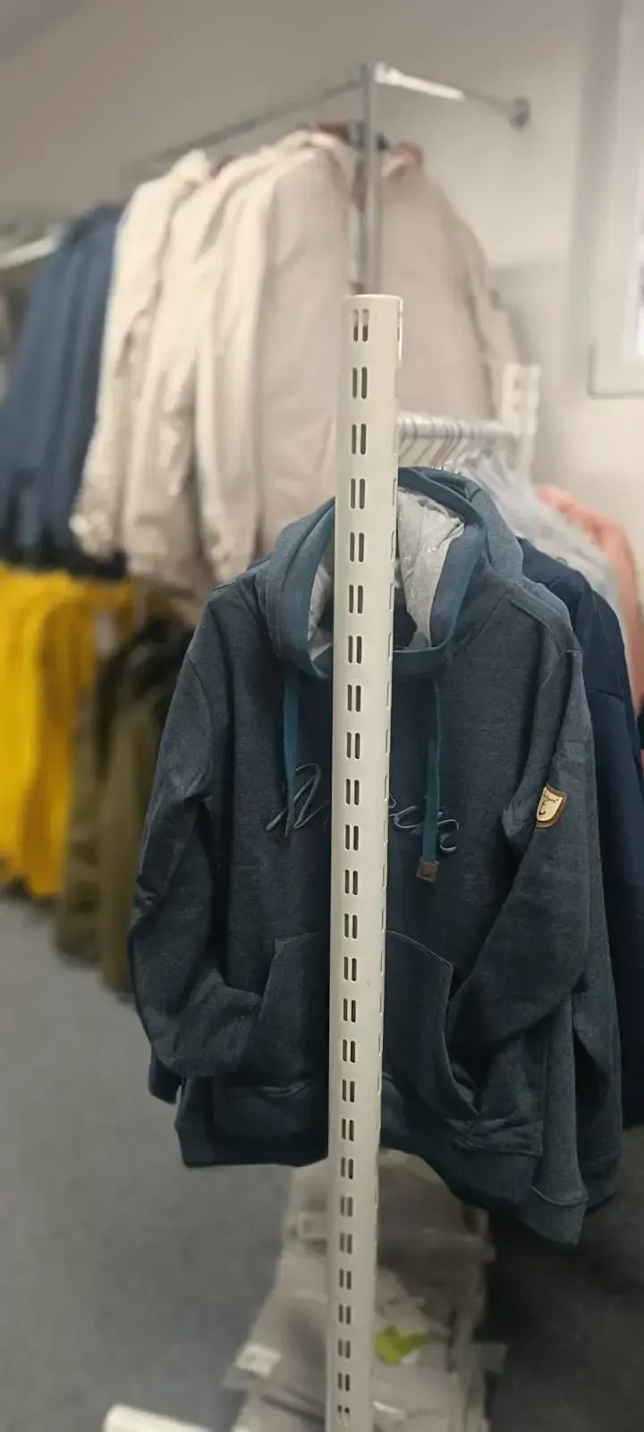 Kleidung hängt an einem Kleiderständer, vorne blaue Jacken, dahinter weiße und gelbe Kleidungsstücke.