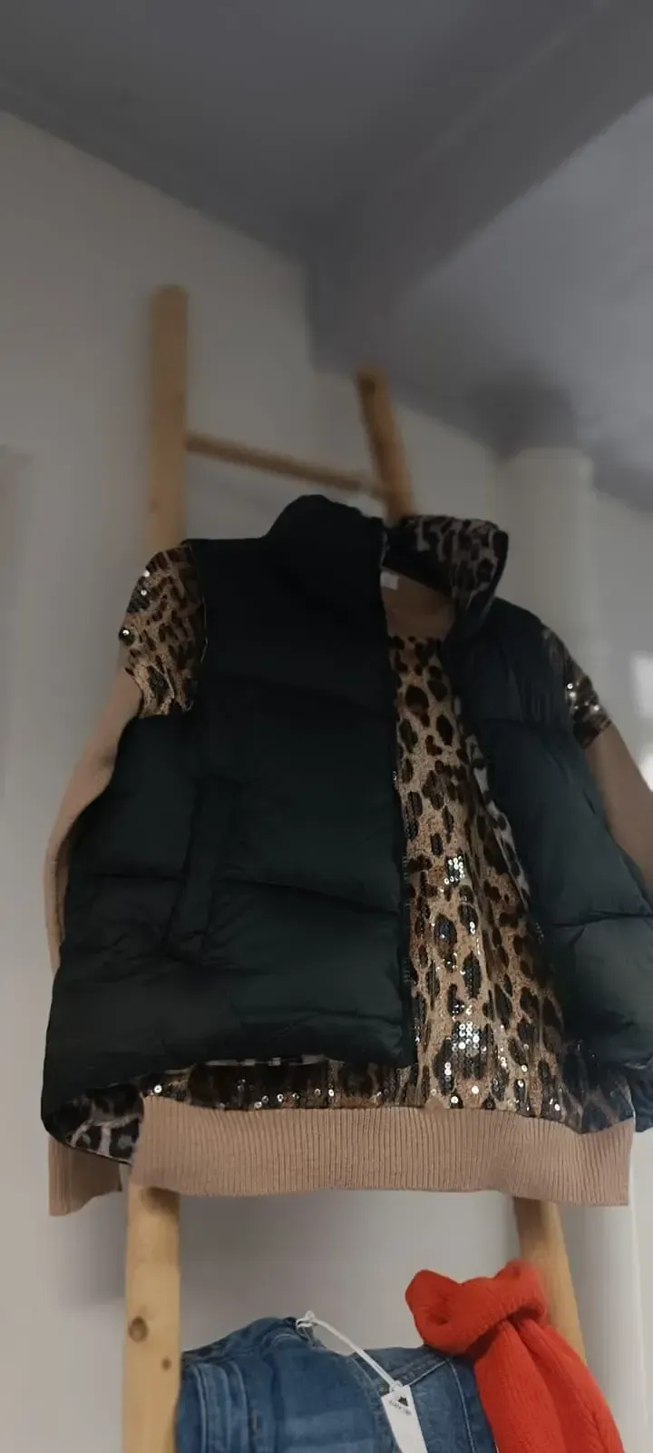 Garderobenständer mit schwarzer Jacke und Leopardenmantel, die an einer Holzleiter hängen, darunter ein orangefarbener Gegenstand.