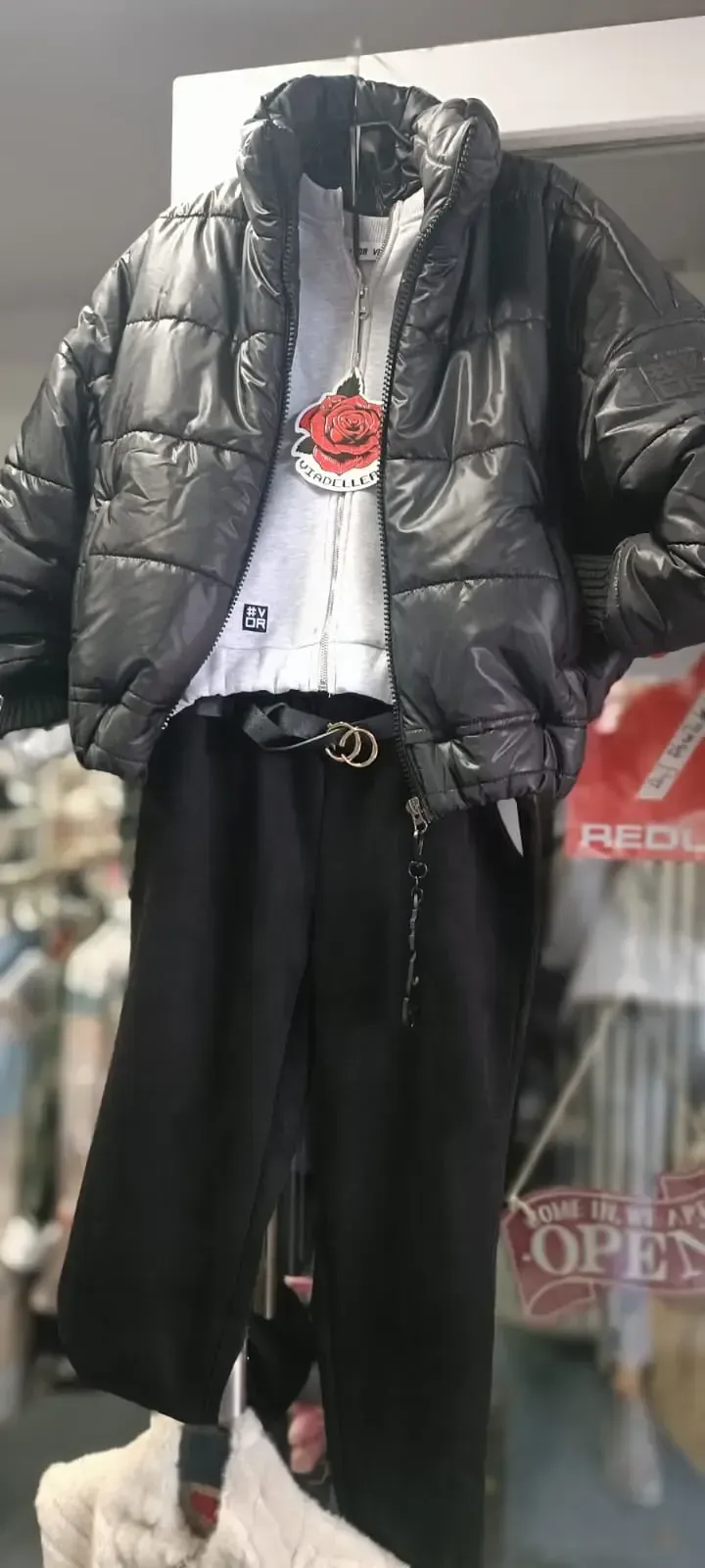 Schwarze Daunenjacke über weißem Hemd und schwarzer Hose, ausgestellt an einer Schaufensterpuppe in einem Schaufenster