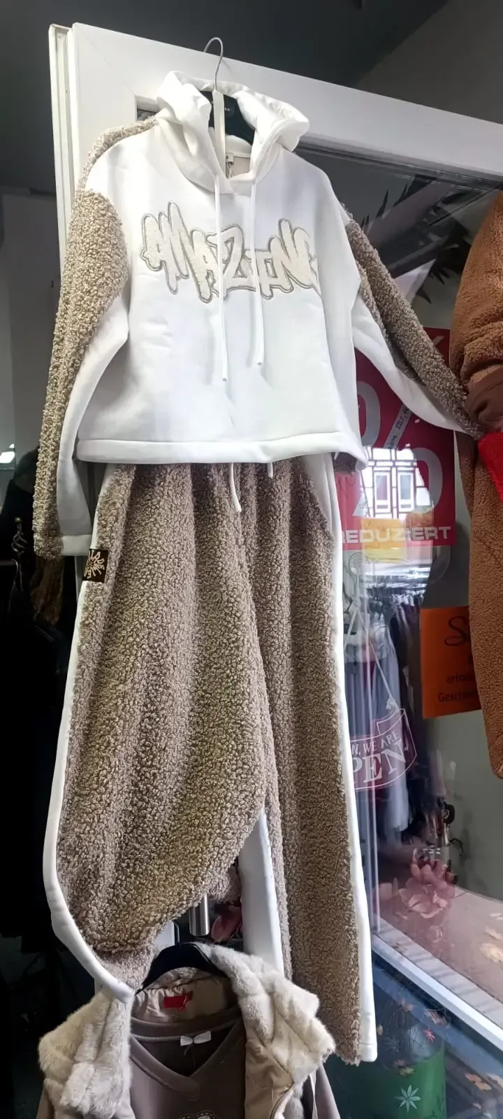 Ein weißer Kapuzenpullover und eine gemusterte Hose werden auf einer Schaufensterpuppe in einem Schaufenster ausgestellt.