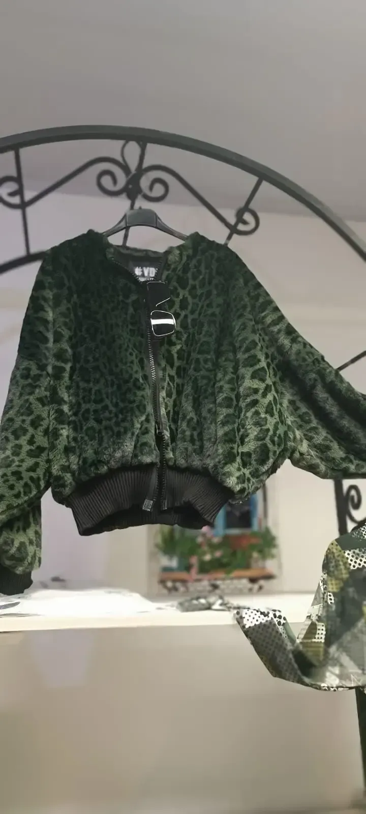 Eine grüne Jacke mit Leopardenmuster und schwarzem Besatz hängt an einem dekorativen Metallbogen.