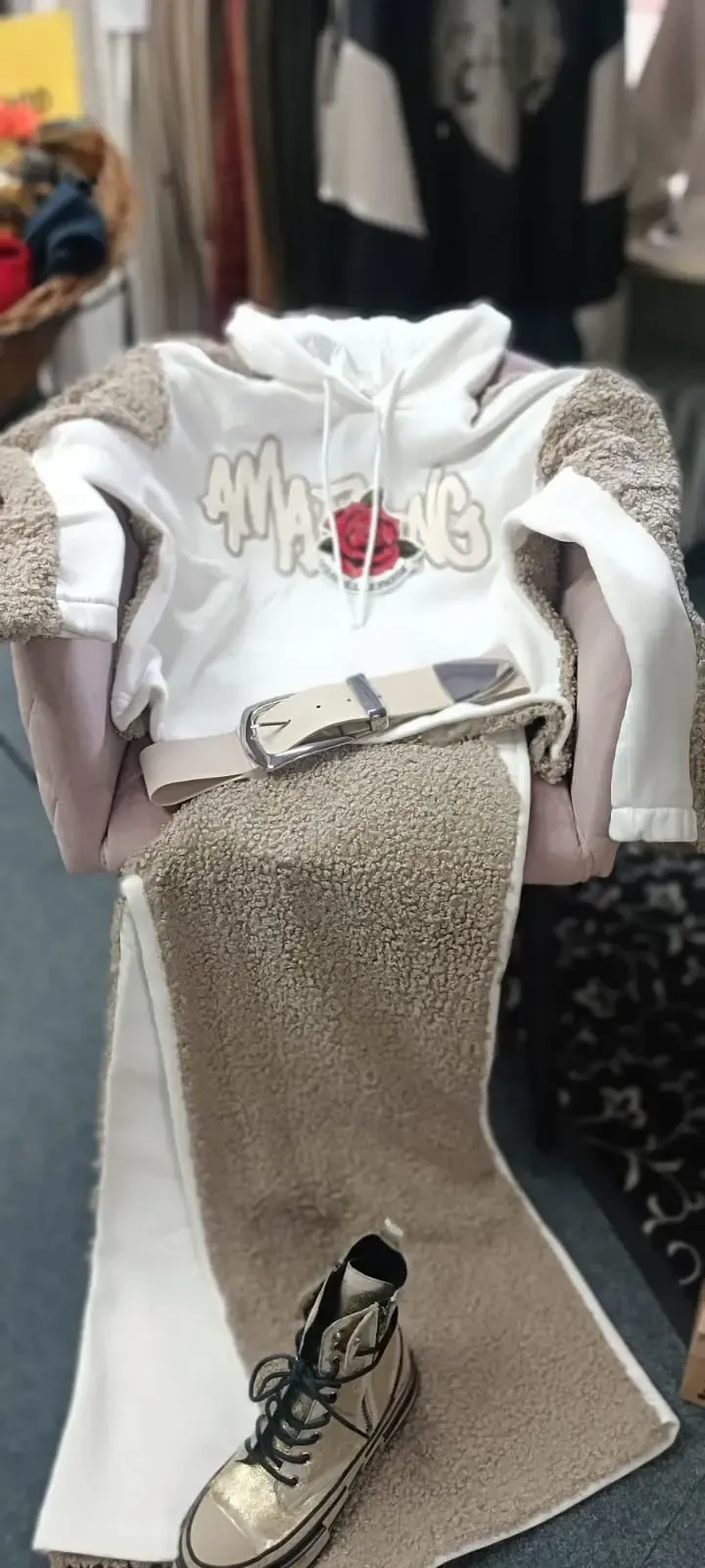 Weißer Kapuzenpullover mit Aufdruck, beiger Rock und Turnschuhe, ausgestellt an einer Schaufensterpuppe in einem Bekleidungsgeschäft.