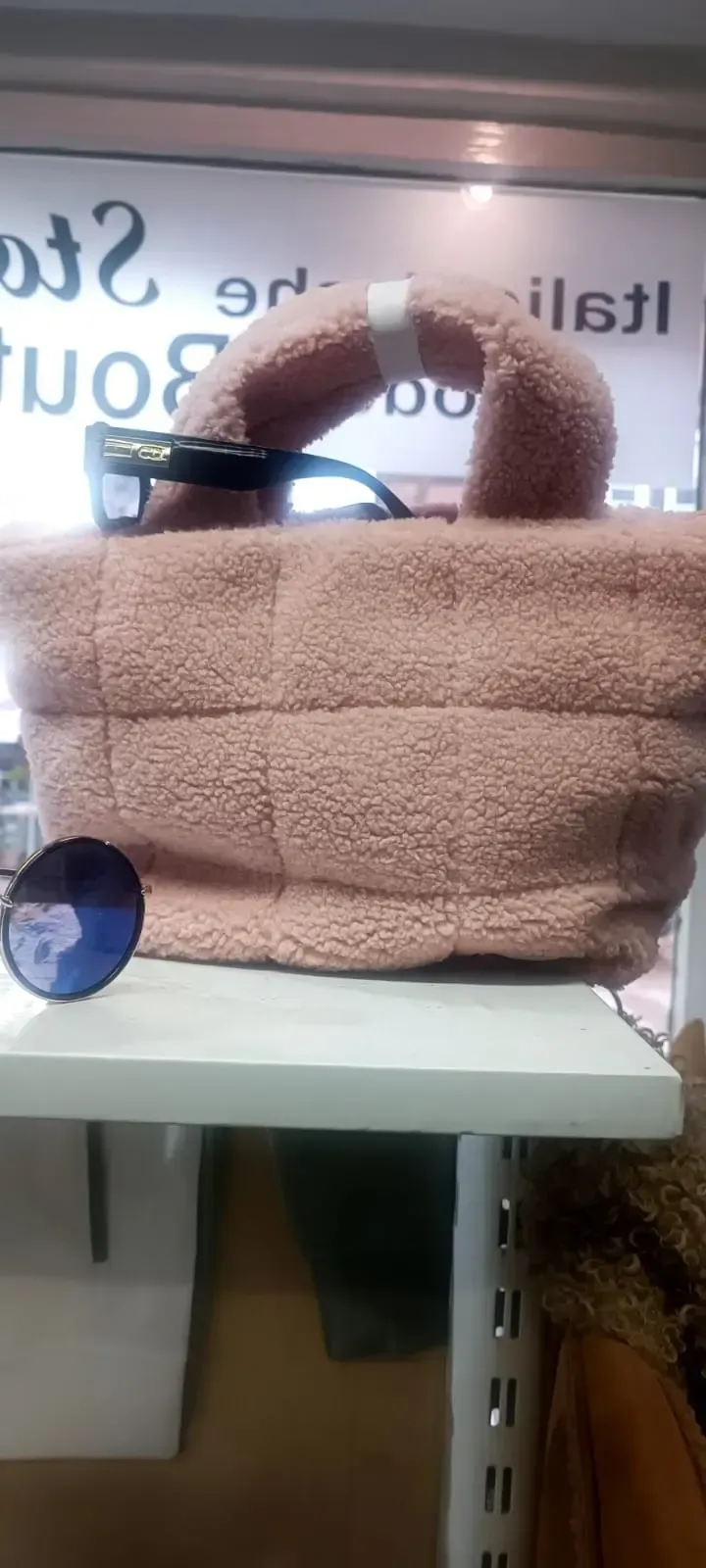 Beigefarbenes, flauschiges Katzenbett oder Transportbox für Haustiere auf einem weißen Regal am Fenster mit Aufklebern.