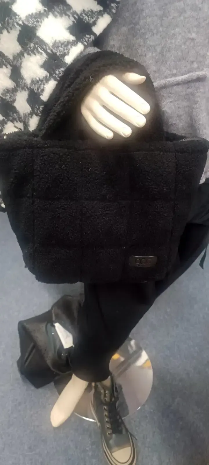 Schwarzer Rucksack mit einer behandschuhten Hand, die in die obere Tasche greift, vor grauem Hintergrund.