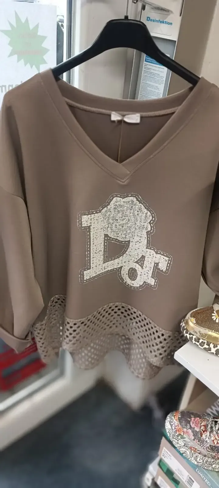 Taupefarbener V-Ausschnitt-Pullover mit weißem, juwelenbesetztem Hundemotiv, der an einem schwarzen Kleiderbügel hängt