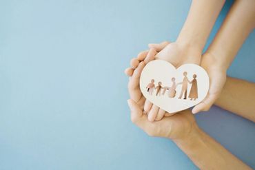 Des mains tenant un cœur blanc avec des silhouettes de famille sur un fond bleu clair