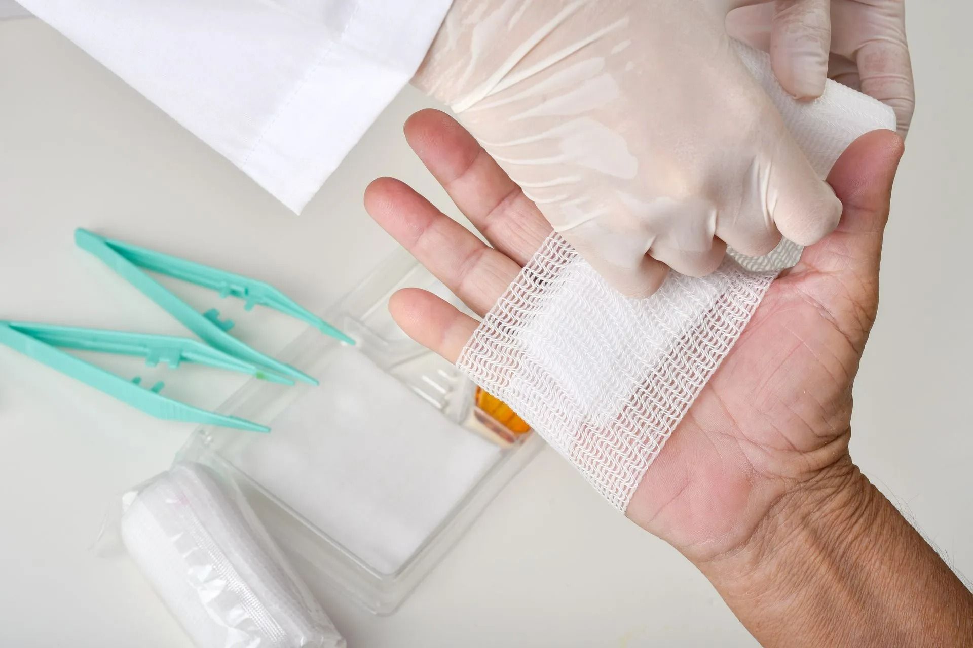 Des mains gantées appliquent un bandage de gaze sur une paume à côté de matériel médical