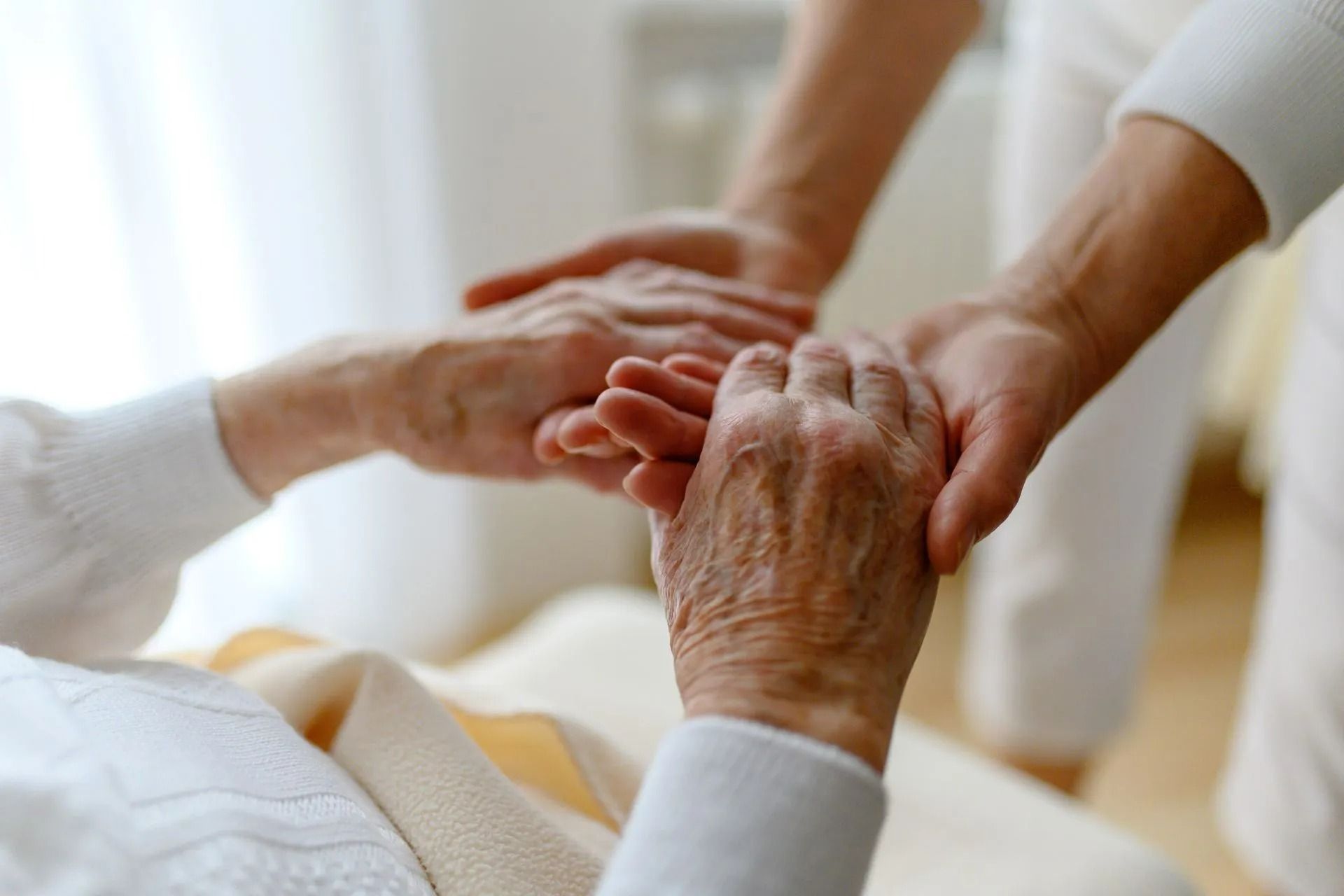Des mains tenant doucement celles d'une personne âgée dans une scène chaleureuse et réconfortante au chevet de son lit