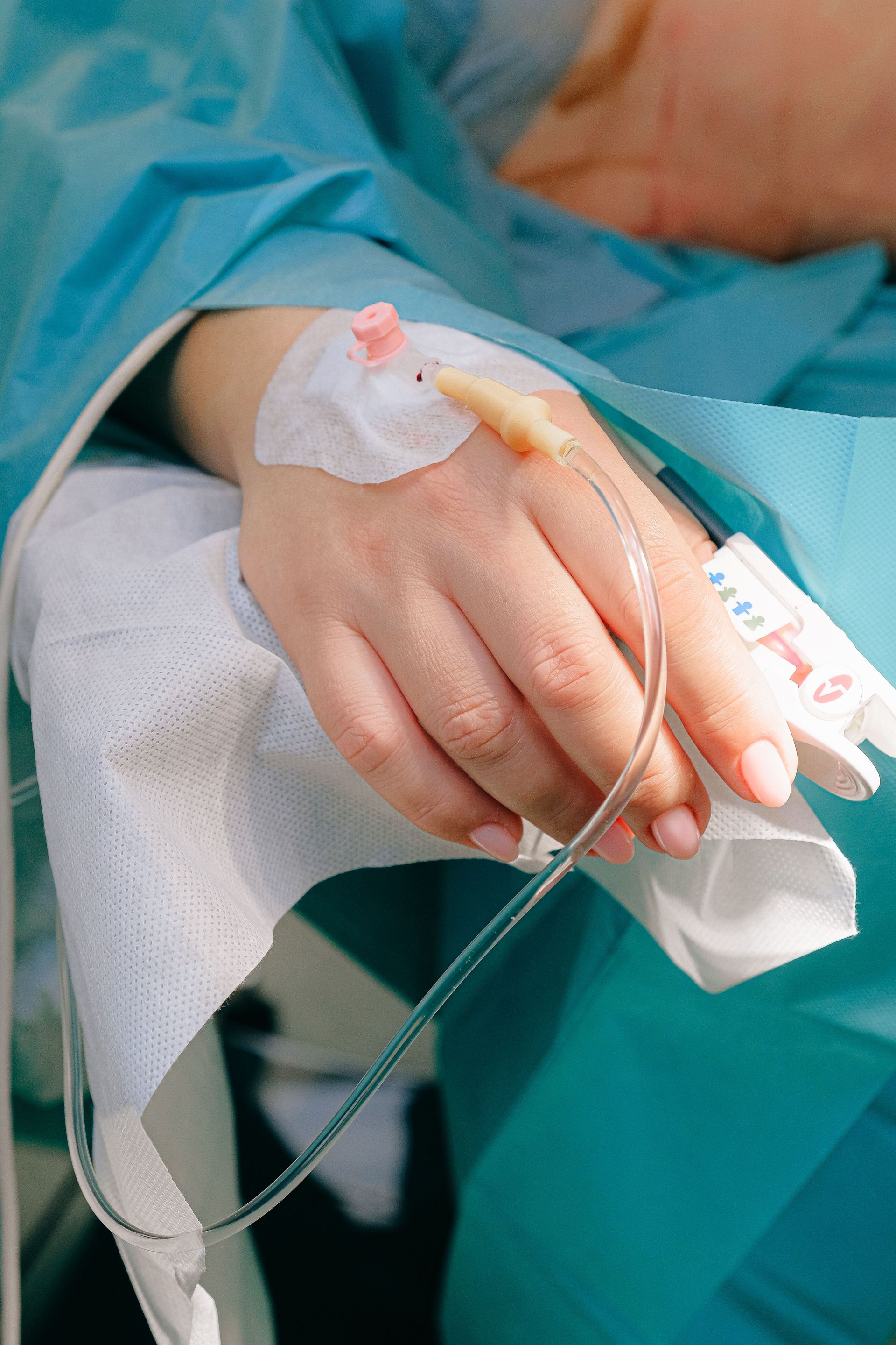 Main avec perfusion et bandage, posée sur un linge blanc sous une blouse chirurgicale bleue