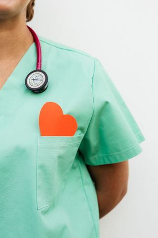 Agent de santé en blouse vert menthe avec un stéthoscope et un cœur orange dans la poche