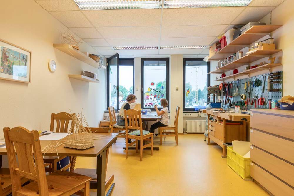 Helles Esszimmer mit Holztischen, Stühlen, Regalen und großen Fenstern nach hinten
