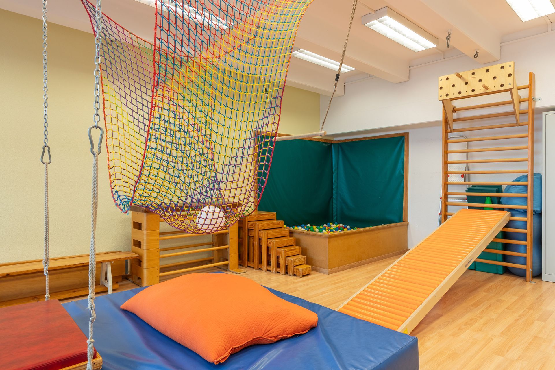 Indoor-Fitnessstudio mit Kletternetz, Leiter, Rampe und blauen Matten mit orangefarbenem Polster.