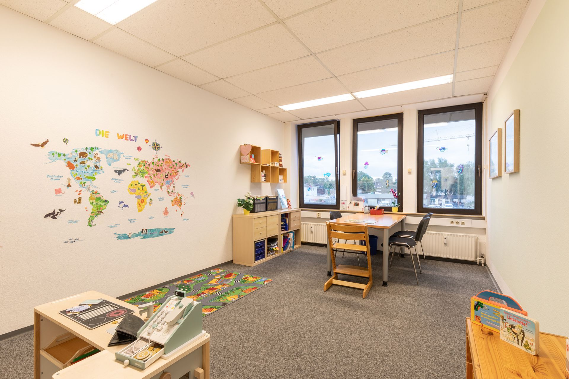Helles Kinderspielzimmer mit Spielzeug, Regalen, farbenfroher Wandgestaltung und einem Weltkarten-Wandbild