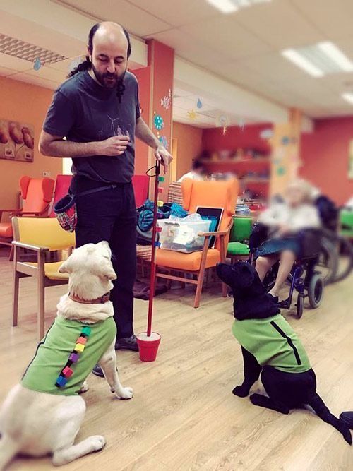 Un hombre está de pie junto a dos perros, uno de los cuales lleva una camisa verde.
