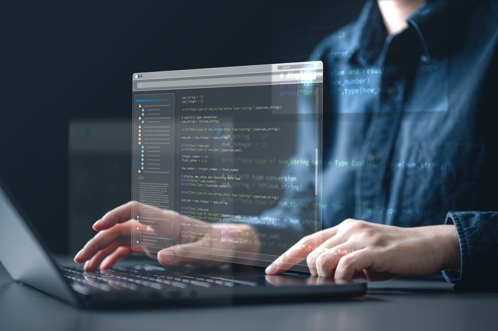 Persona tecleando en un portátil con una superposición de editor de código transparente en una oficina con poca luz.