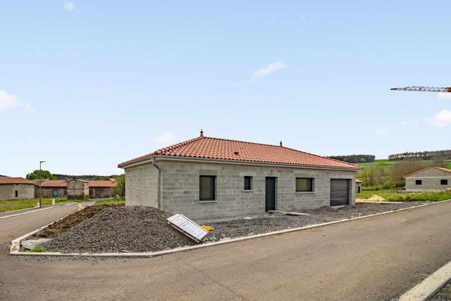 Maison en pierre de construction récente avec toit de tuiles rouges, située sur une route pavée dans un quartier calme.