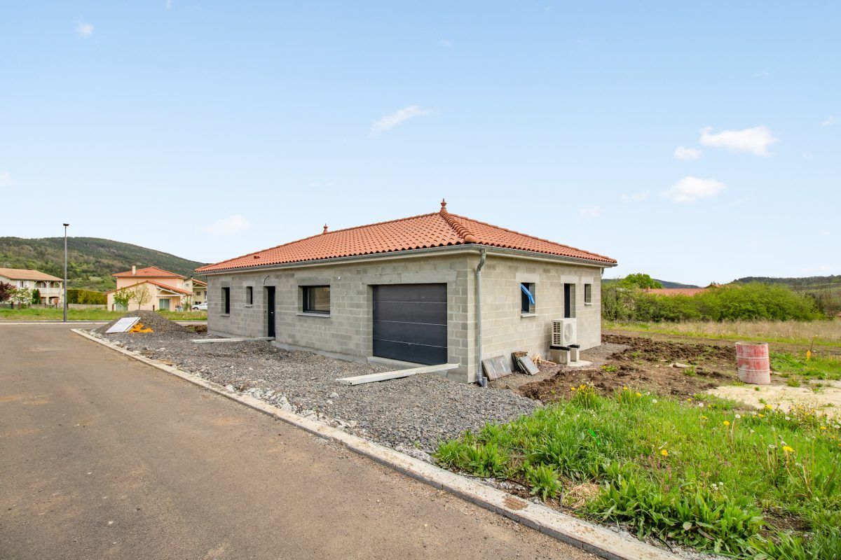 Maison de plain-pied au toit de tuiles rouges, située au bord d'une route goudronnée en zone rurale.