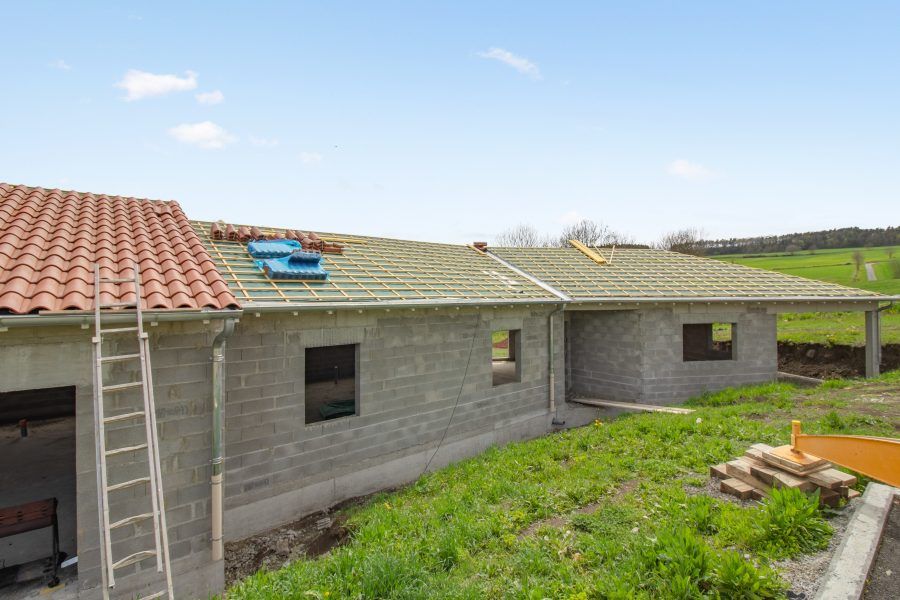 Maison grise de plain-pied avec toits de tuiles et cour gazonnée sous un ciel bleu