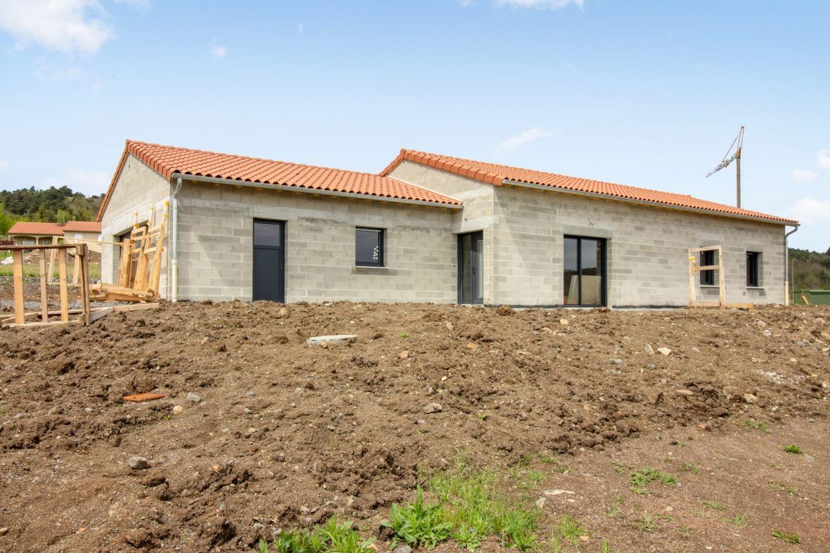 Maison neuve de plain-pied avec toit de tuiles rouges sur un terrain en terre battue en construction