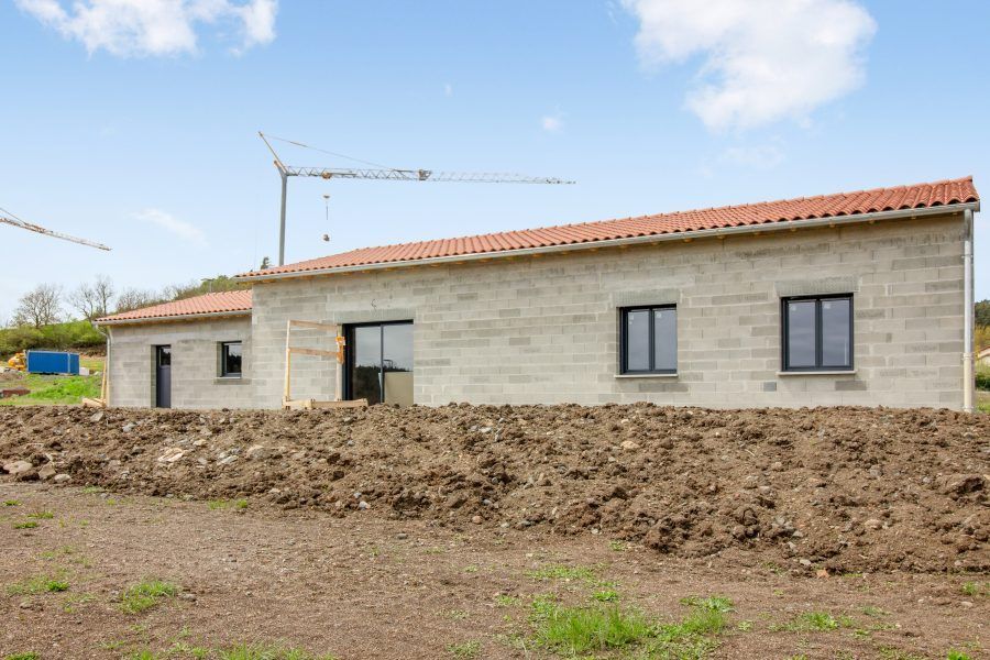 Maison inachevée de plain-pied aux murs de pierre grise, au toit rouge et au premier plan de terre sous un ciel bleu