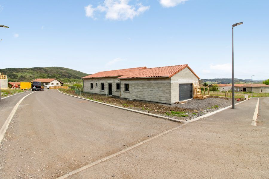 Route goudronnée longeant une rangée de petites maisons sous un ciel bleu, avec des collines à l'horizon.