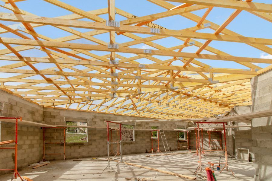 Intérieur d'un bâtiment en construction avec charpente apparente en bois, murs en parpaings et échafaudages.