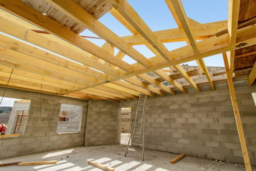 Intérieur d'une maison en construction avec des murs en parpaings, des poutres de toit en bois apparentes et une échelle.