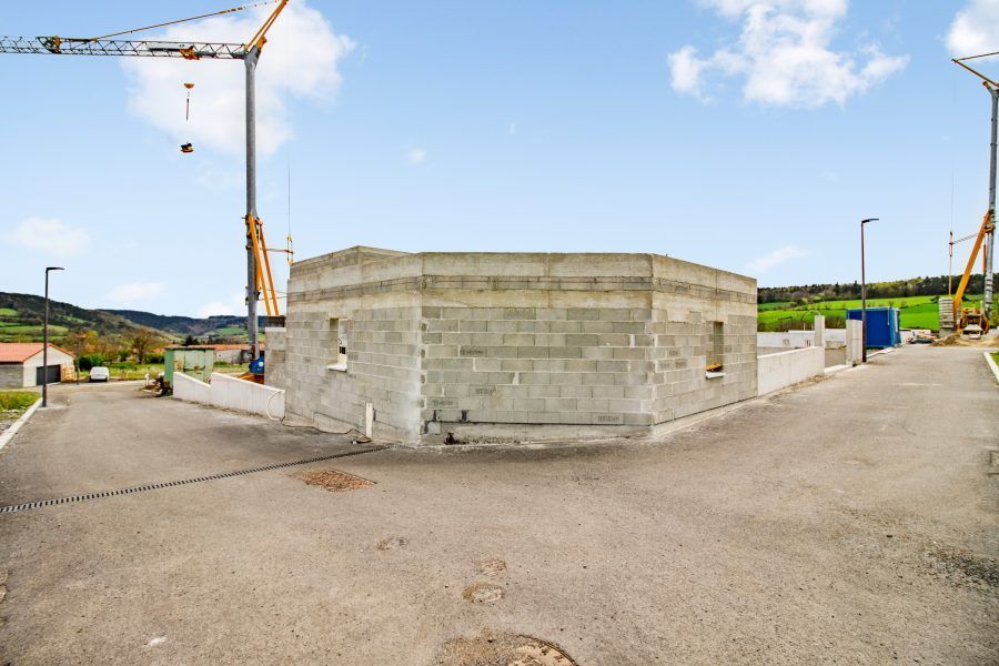 Chantier de construction avec un bâtiment en parpaings, une grue et une aire pavée ouverte sous un ciel bleu