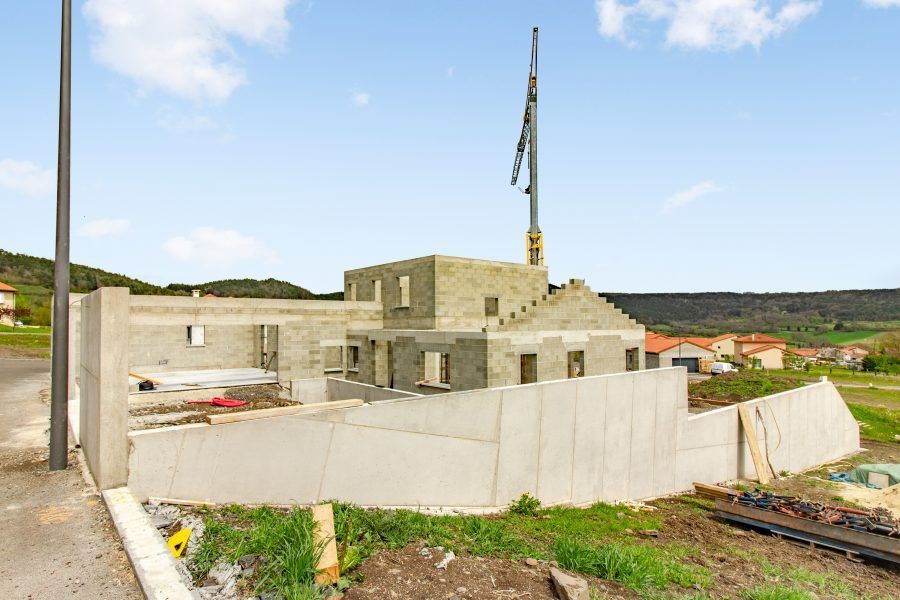 Maison en pierre partiellement construite, avec un mur blanc et un mât de drapeau, sur une colline rurale.