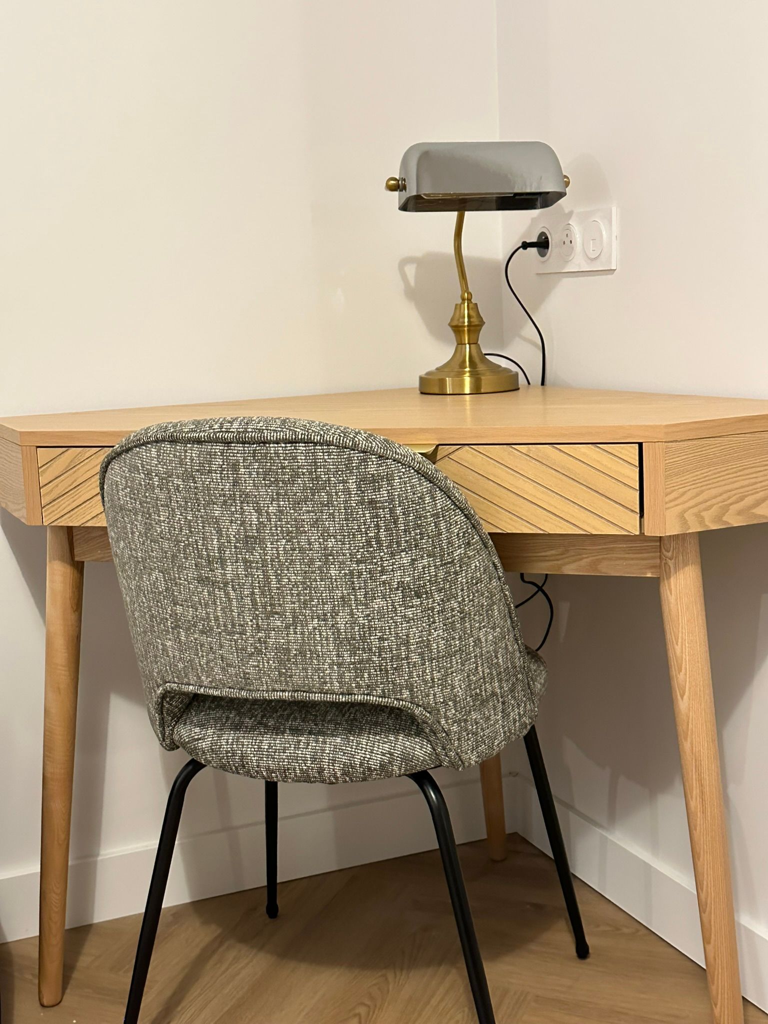 Petit bureau dans un coin avec une chaise grise et une lampe en laiton dessus.