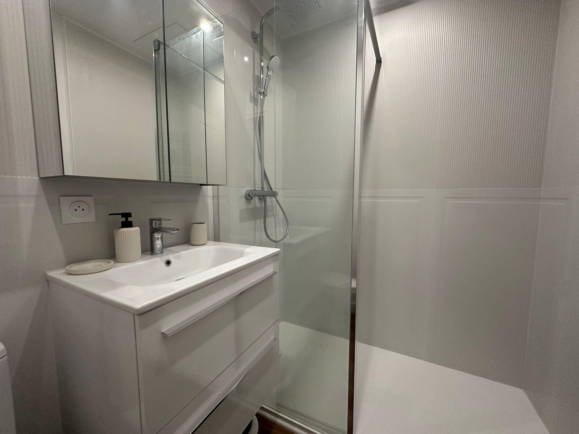 Salle de bains moderne blanche avec meuble-lavabo, miroir, douche et paroi en verre