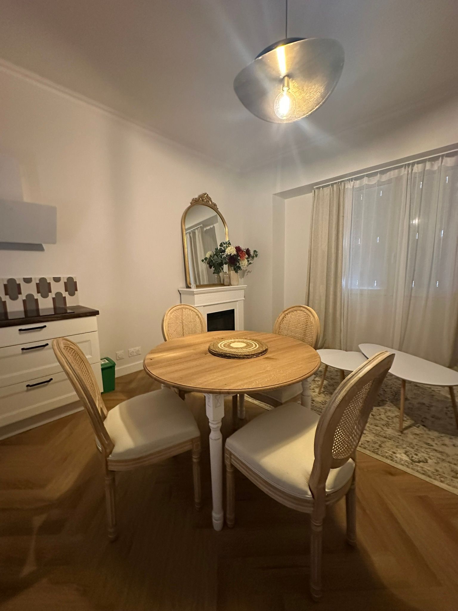 Salle à manger chaleureuse avec table ronde en bois, chaises couleur crème, canapé, miroir et éclairage tamisé