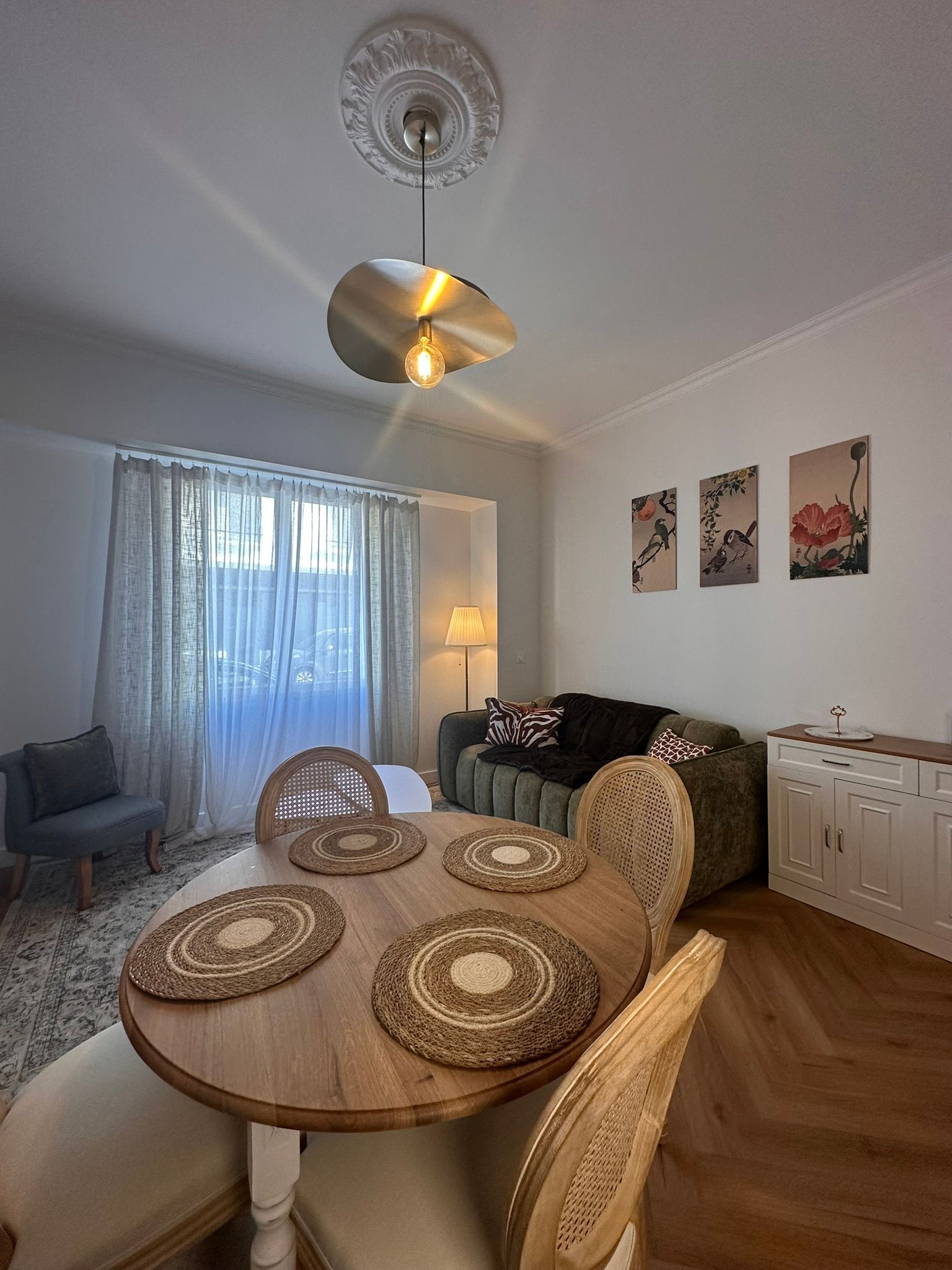 Salle à manger avec table ovale, chaises en osier, voilages et décorations murales dans un appartement lumineux