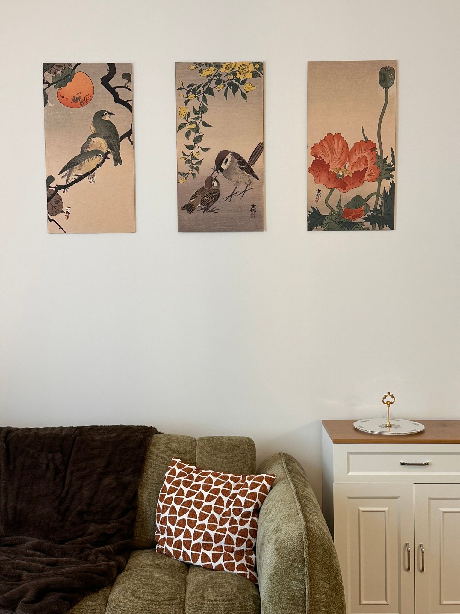 Salon cosy avec des tableaux, un canapé foncé, des coussins à motifs et une table d'appoint blanche.