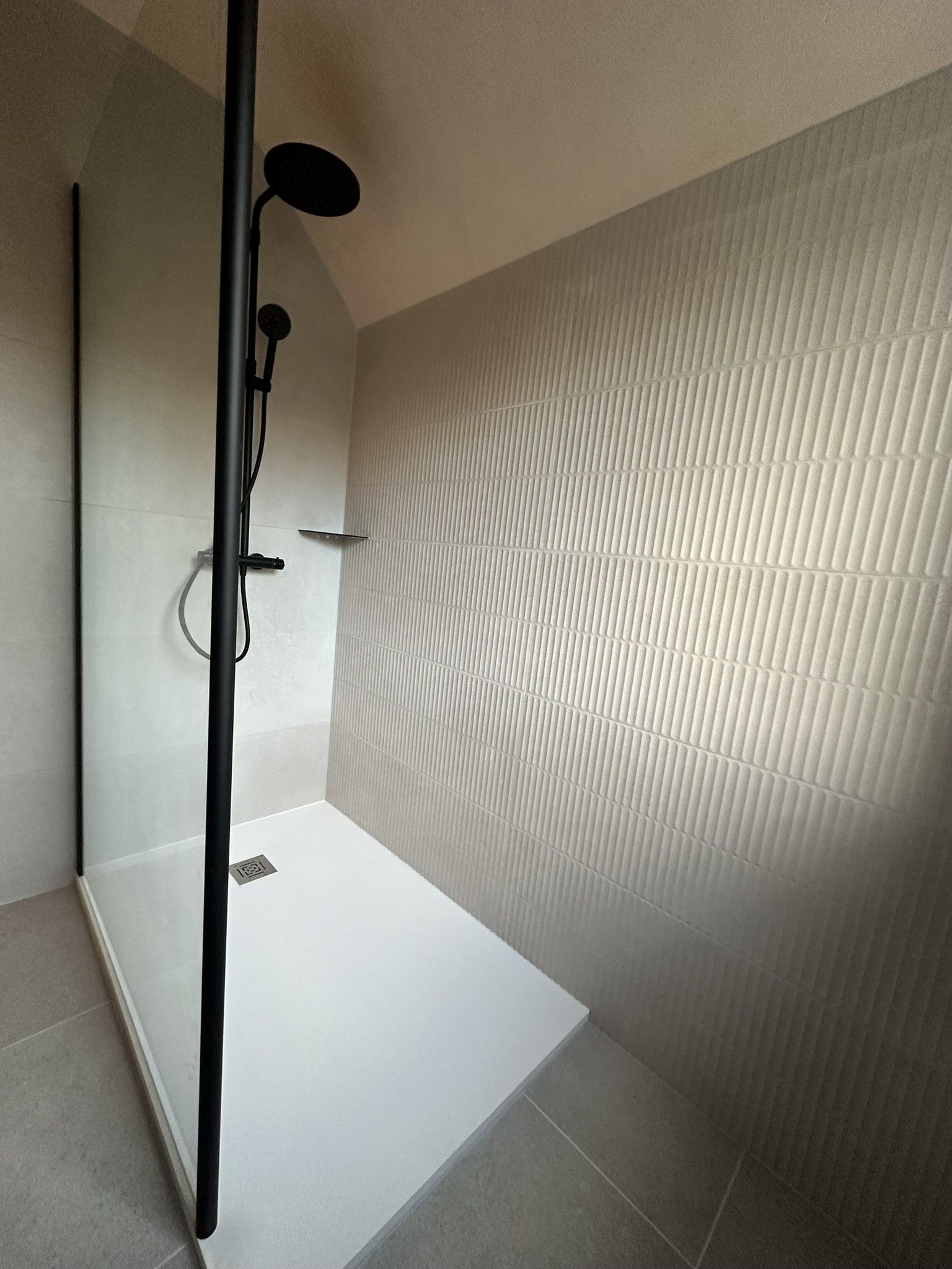 Douche à l'italienne avec robinetterie noire et murs texturés blancs et gris