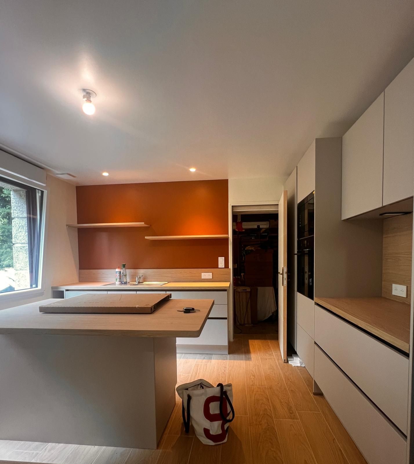 Intérieur de cuisine moderne avec armoires blanches, parquet, îlot et mur d'accent orange