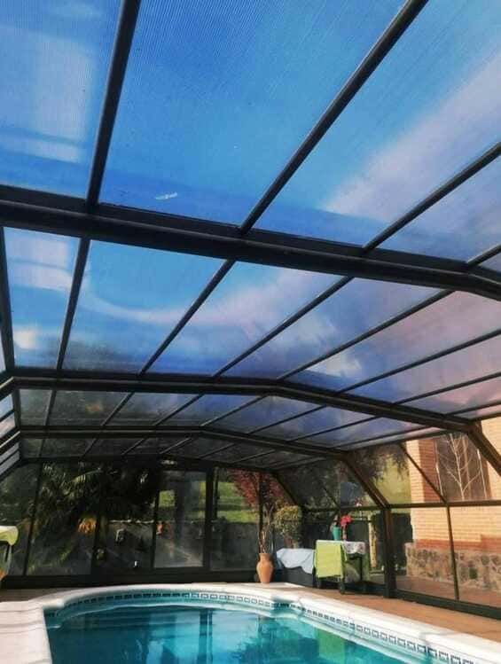Una piscina bajo un techo transparente con un cielo azul de fondo.