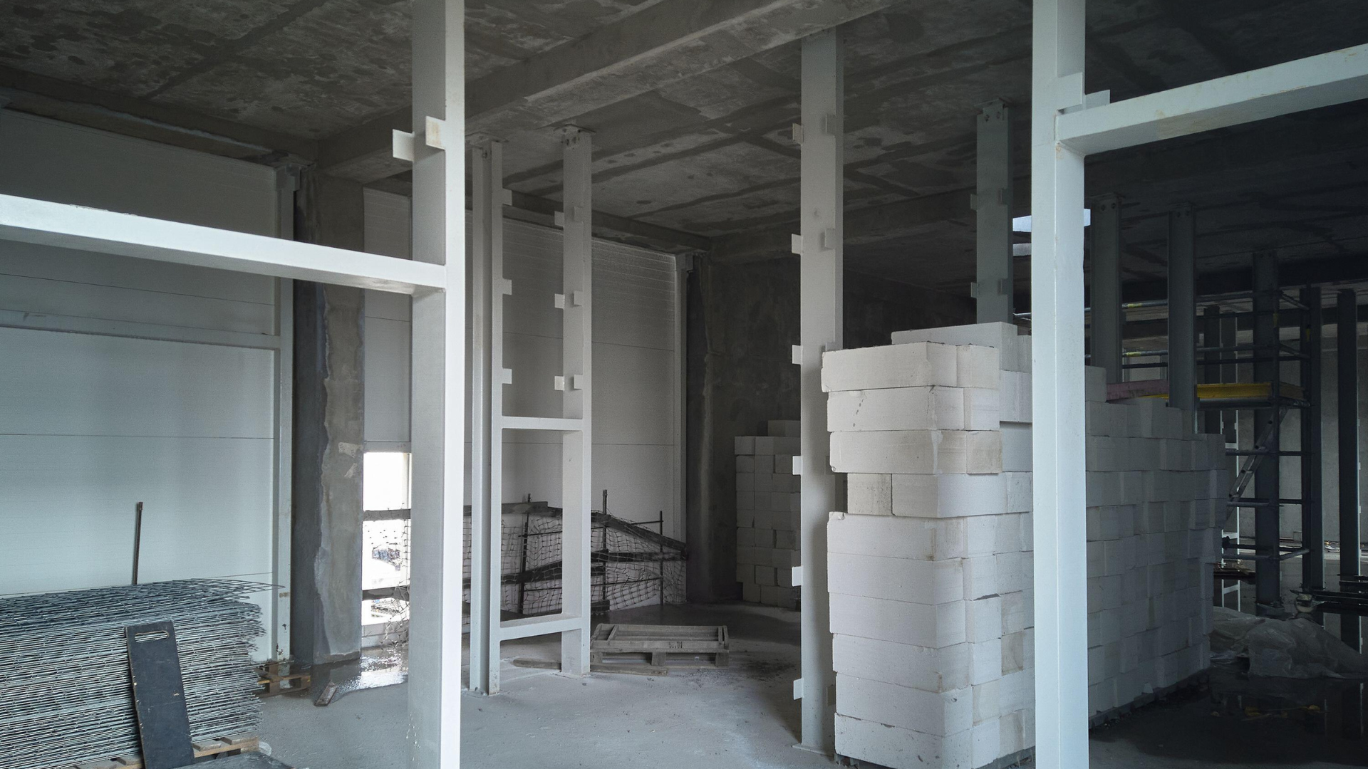 Intérieur d'un bâtiment en construction avec piliers en béton, supports blancs et blocs empilés.