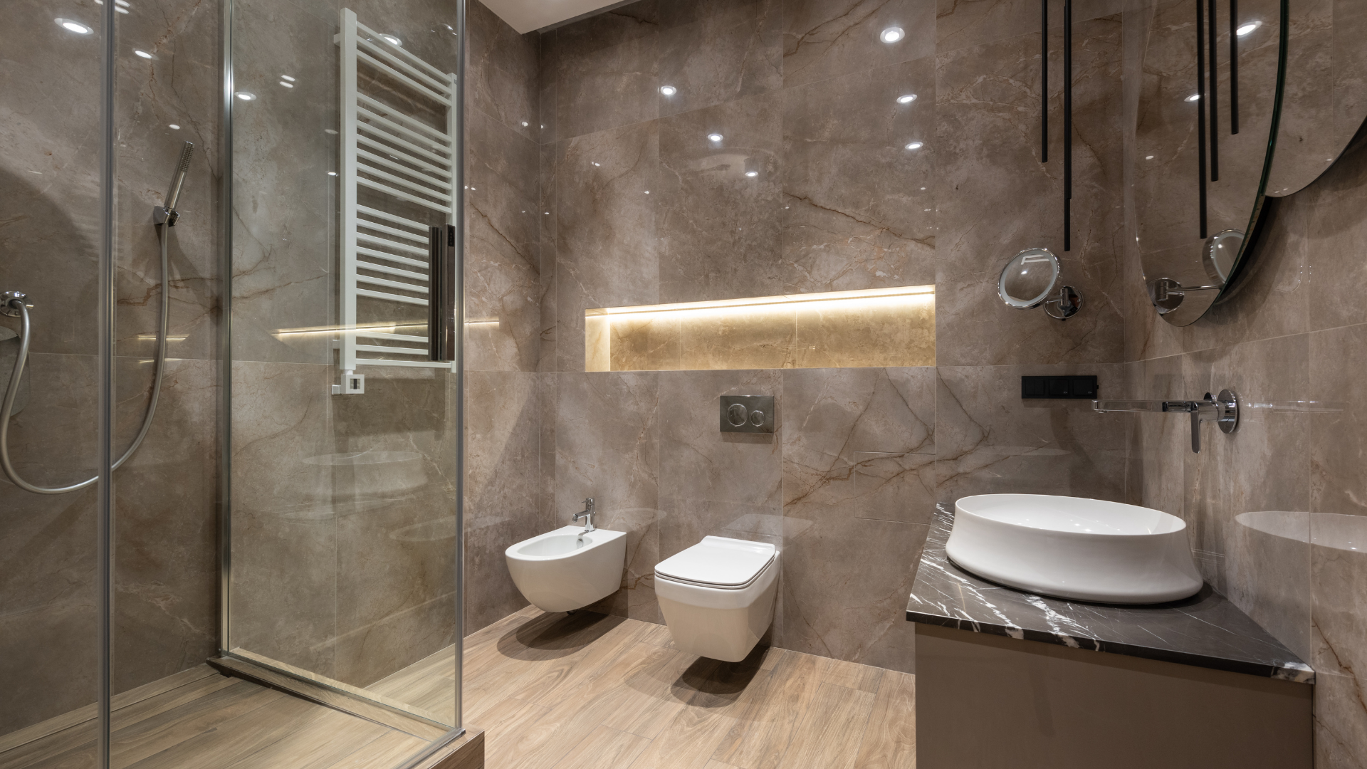 Salle de bain moderne avec murs aspect marbre, douche en verre, toilettes flottantes, lavabo et couleurs neutres.
