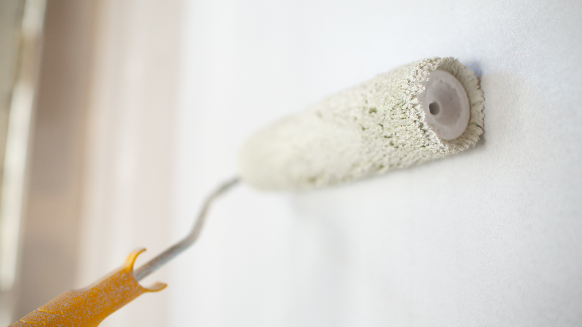 Un rouleau à peinture, de couleur beige clair, applique de la peinture sur un mur blanc.