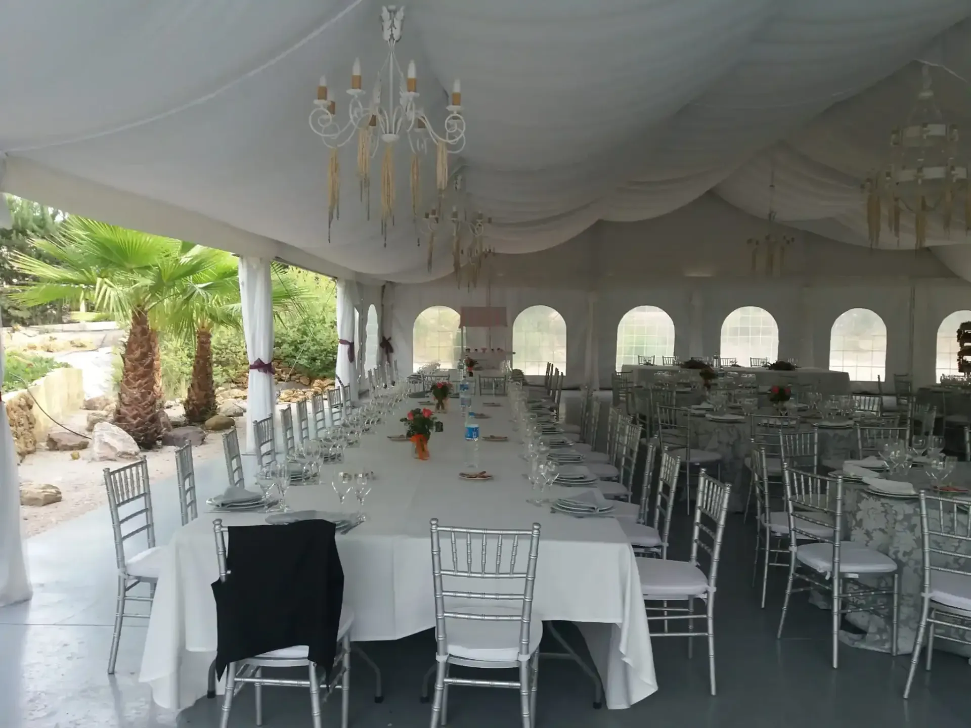 Una mesa larga dispuesta para un evento formal en una carpa blanca con candelabros.