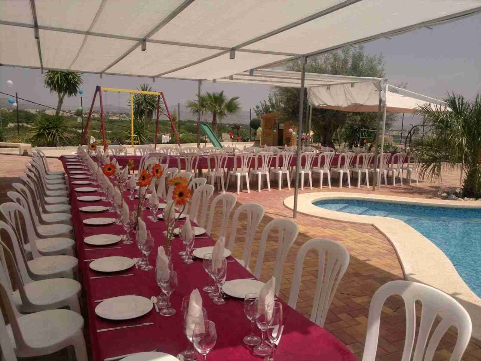 Largas mesas dispuestas para comer bajo un dosel, al lado de una piscina.