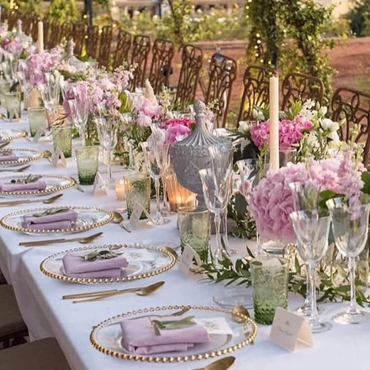 Mesa de comedor para exterior larga y elegante con flores, velas y cristalería.